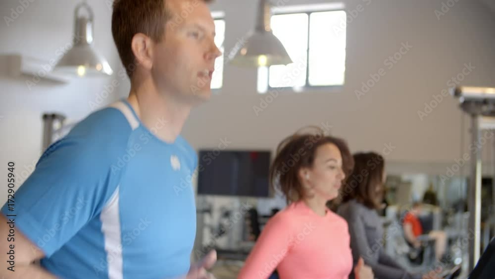 Man and two young women running on treadmills at a gym Man and two young women running on treadmills at a gym