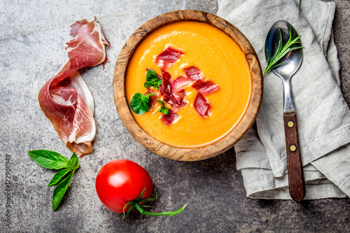 Spanish tomato soup Salmorejo served in olive wooden bowl with ham jamon serrano on stone background. Top view photo