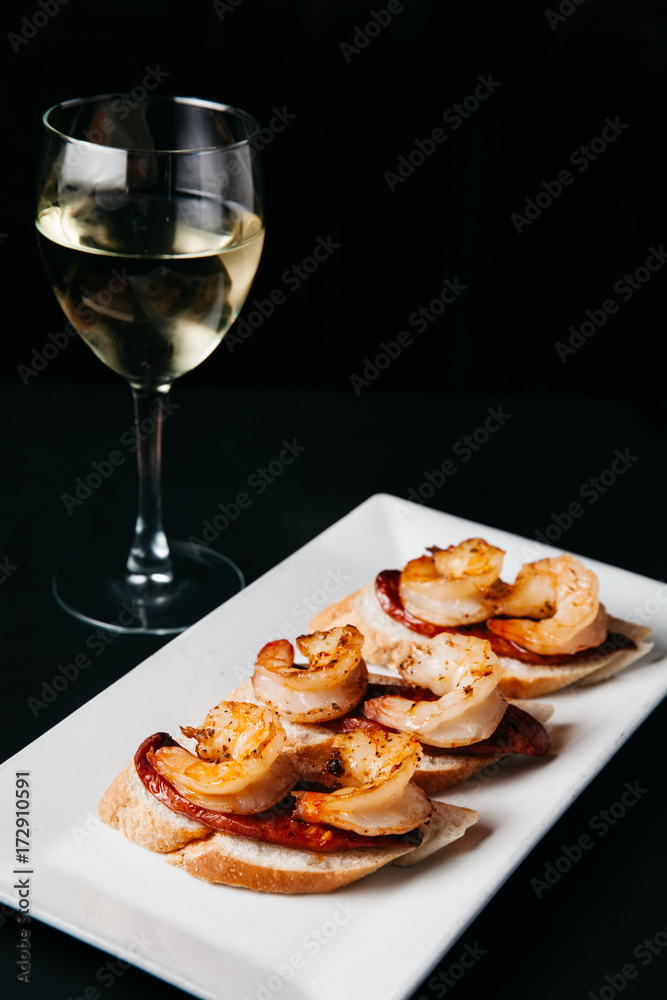 Plate of delicious bruschetta with grilled shrimp and sausage on dark background Plate of delicious bruschetta with grilled shrimp and sausage on dark background