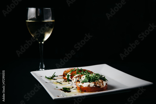 Caprese Salad on a white plate with a glass of white wine  horisontal with dark negative space