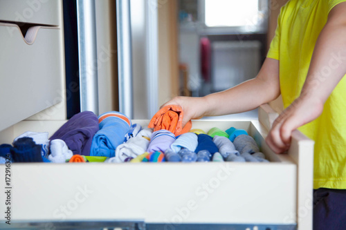 The child puts his clothes on. The boy pulls the T-shirt out of the closet. photo