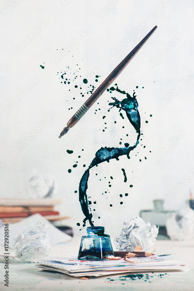 Spilled ink flying above inkwell in a spiraling splash with tiny drops and flying pen on a light background. Still life with writer workplace. Creative writing concept. - obrazy, fototapety, plakaty 