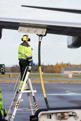 Bild auf Leinwand Male Worker Refueling Airplane While Standing On Ladder