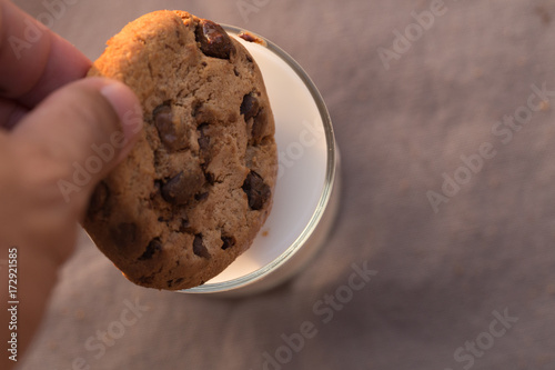 chocolate chips cookie and a glass of milk on brown background