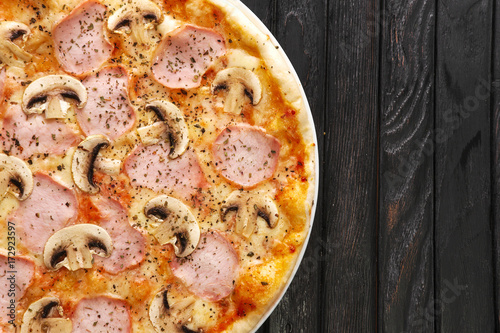 Top view of tasty pizza with ham and mushroom on dark wooden background