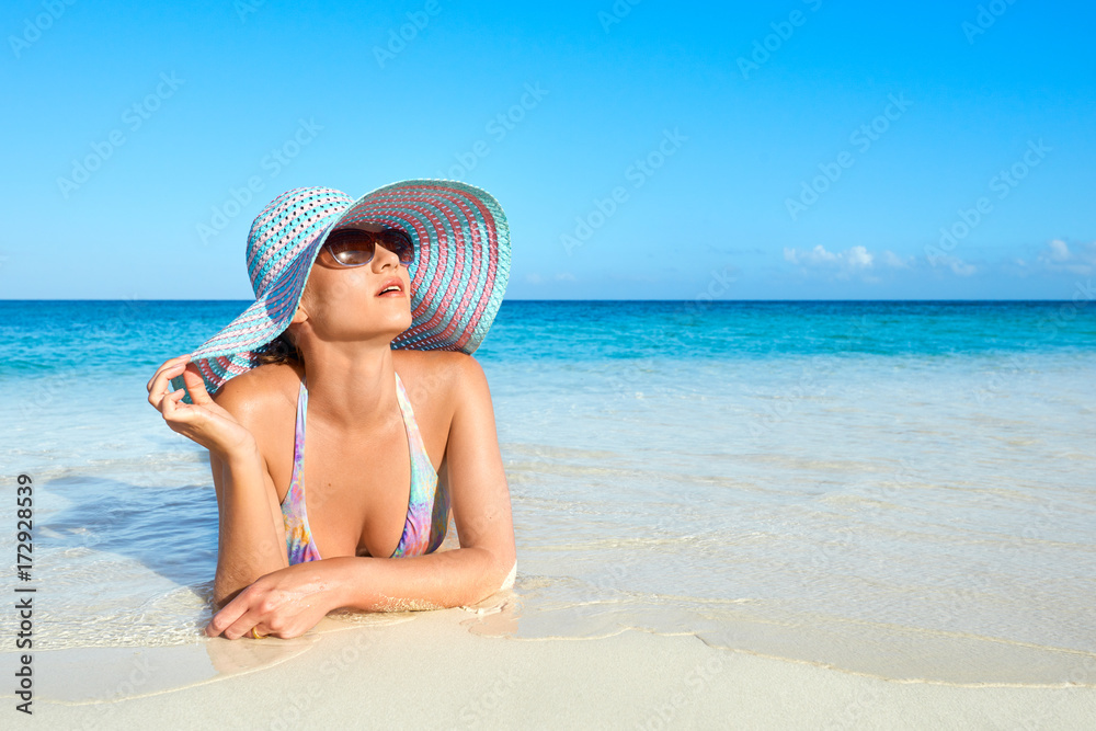 Relaxing woman in bikini and summer hat enjoying the summer sun happy lying on tropical beach