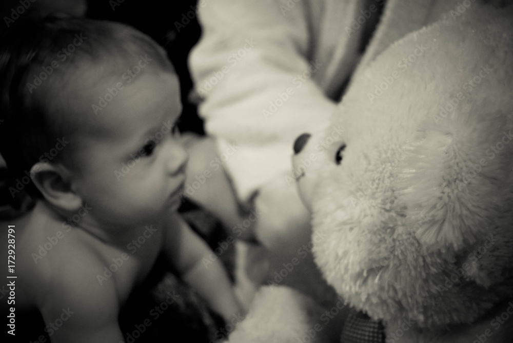 A curious baby with a toy white bear - black and white