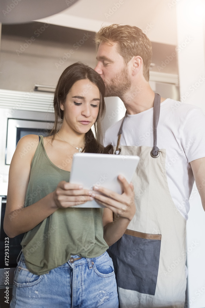 Woman using digital tablet while her husband kissing her at home Woman using digital tablet while her husband kissing her at home