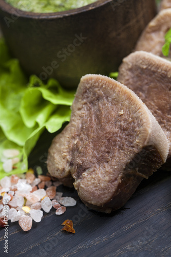 Boiled beef tongue on dark wooden table with pesto and salad photo