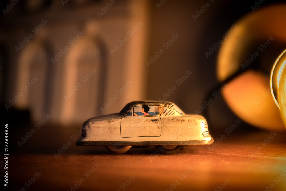 A toy car close up going towards the left with a warm light in the background. The toy is made of metal with two characters painted on it. A toy car close up going towards the left with a warm light in the background. The toy is made of metal with two characters painted on it.