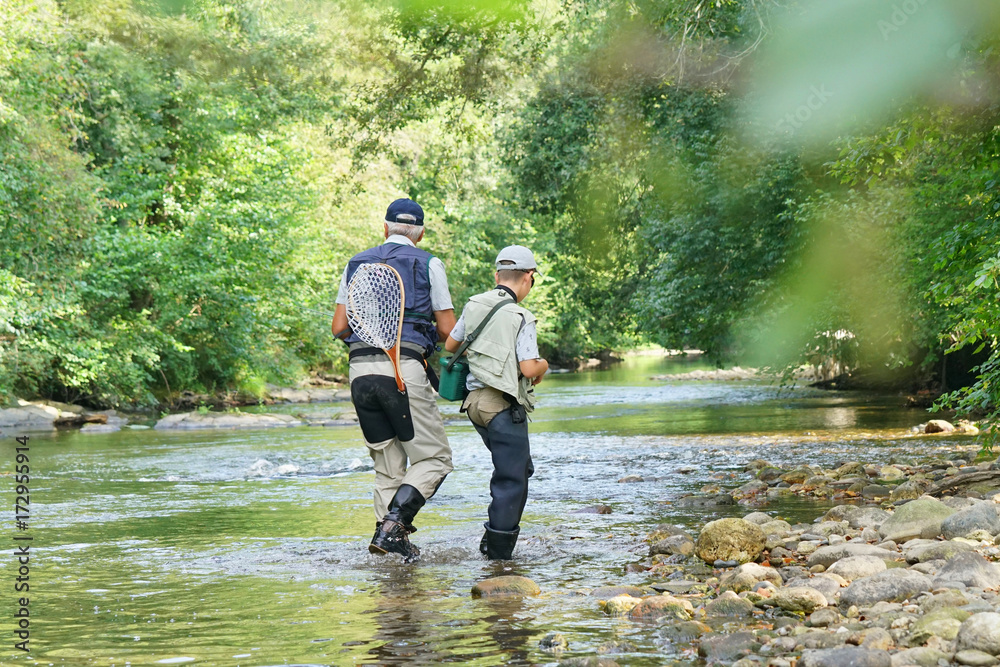 back view of father and son fly-fishing in river back view of father and son fly-fishing in river