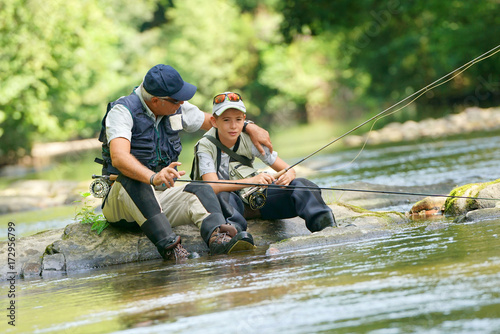 Father and son fly-fishing in river, sitting on rocks photo
