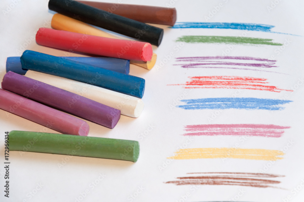 Fototapeta premium A set of multicolored pastel pencils on a light background with a trail drawn next to it. Selective focus