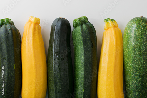 Closeup of yellow and green zucchinis in a row on white table, top view.