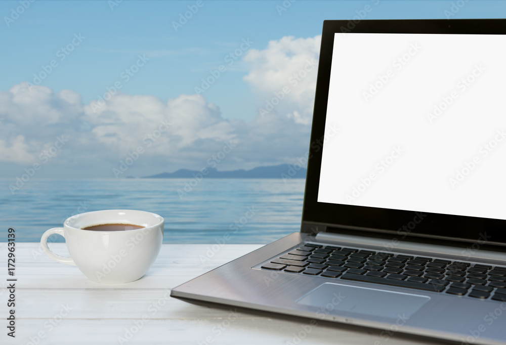Fototapeta premium Outdoor workspace,computer notebook and coffee cup on wooden table with blue sea sky baclground