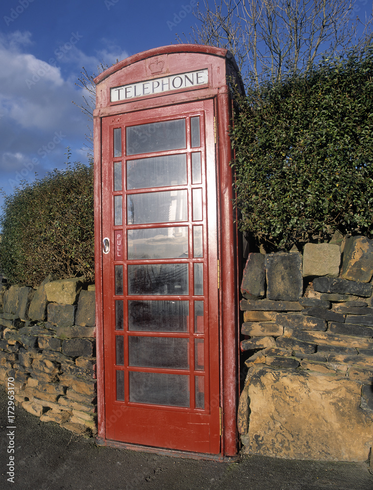 Obraz premium Traditional red telephone kiosk built into brick wall with blue sky