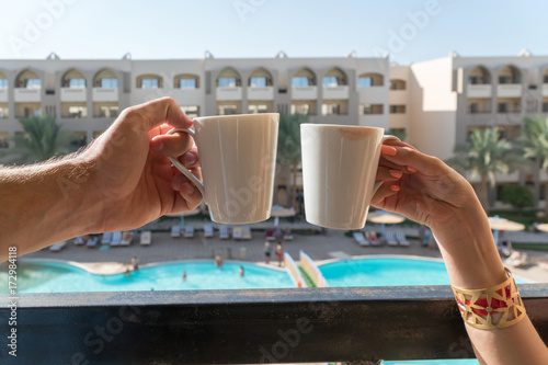 The hands of men and women keep coffee mugs on the balcony in the background of the hotel, where the buildings and the pool are visible photo