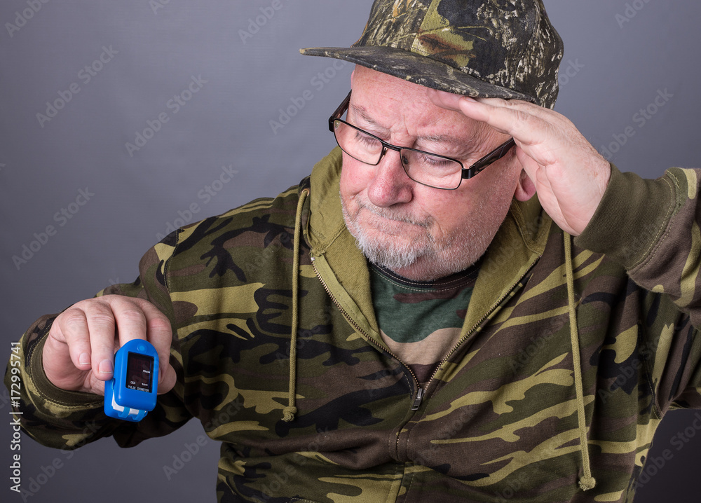 Senior elderly old man wearing camouflage clothing and checking his pulse  and oxygen blood levels with a pulse oximeter Stock-foto | Adobe Stock