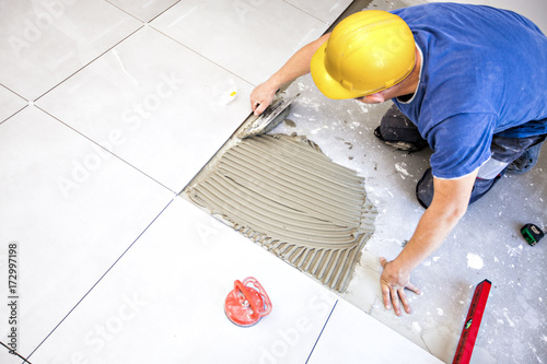 Foto Tile laying tiles at home. Construction worker laid floor tiles.