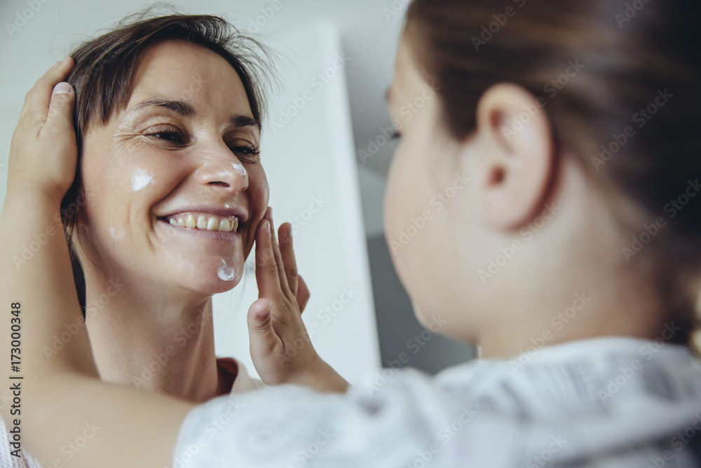 Daughter putting facial cream on mother's face