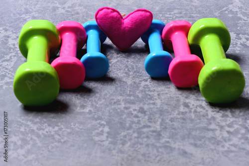 Barbells in different colors and heart placed in pattern, closeup