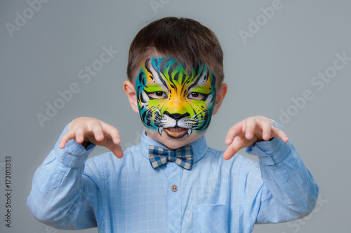 little boy painted like a tiger on a gray background. face painting