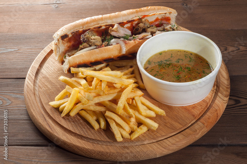 Street food, sandwich with chicken, french fries and bouillon on a wooden board
