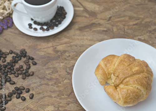 breakfast croissant and cup of coffee put on wood background.