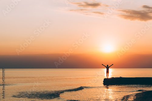 Young woman standing with raised arms looking in sunset