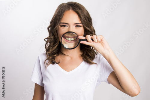 Young girl holding magnifier over her teeth 