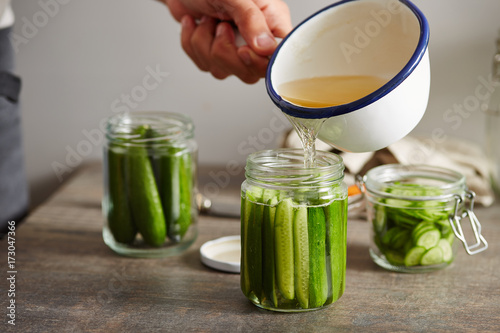 Man's hand pouring pickle in jar with cucumbers photo