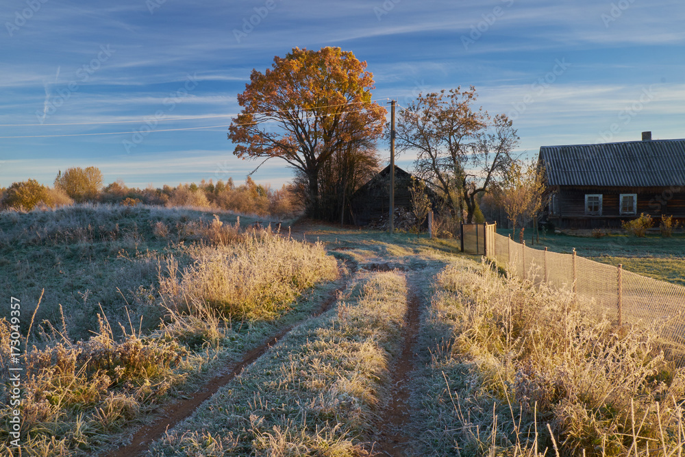 The first frost in autumn, rural landscape with wooden house and track