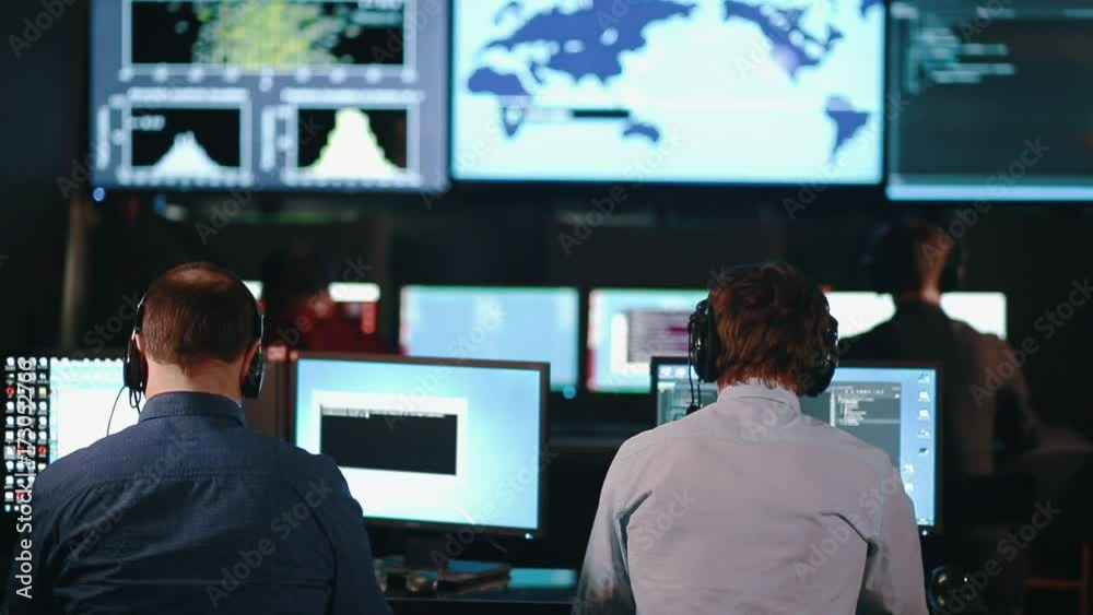 Team of security personnel watching the screens in a system control center. This could be a weather station or airport traffic control room.