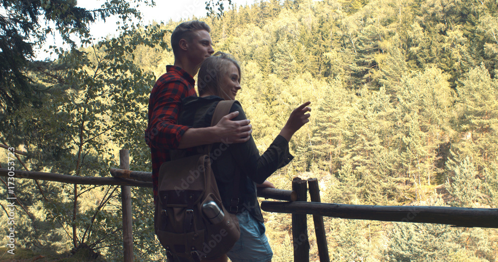 Rear view of hugging couple standing on a hill in a forest. Adventure, travel, tourism, leisure and love concept - loving couple watching beautiful view. Rear view of hugging couple standing on a hill in a forest. Adventure, travel, tourism, leisure and love concept - loving couple watching beautiful view.