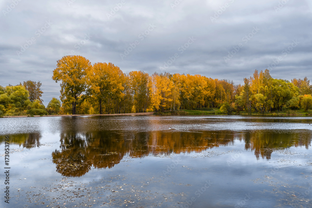 Obraz premium The lake, reflecting the cloudy sky and autumnal foliage trees