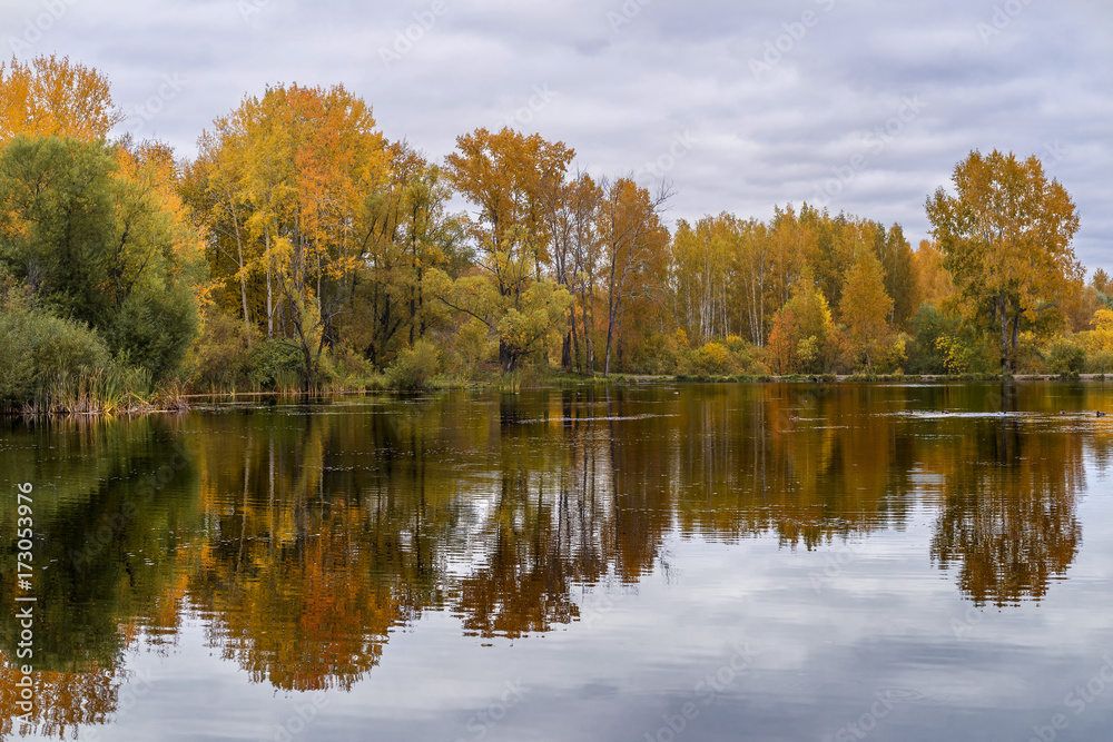 The lake, reflecting the cloudy sky and autumnal foliage trees