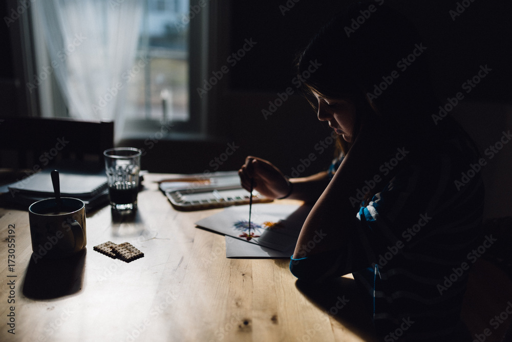 young woman painting at a table by the window