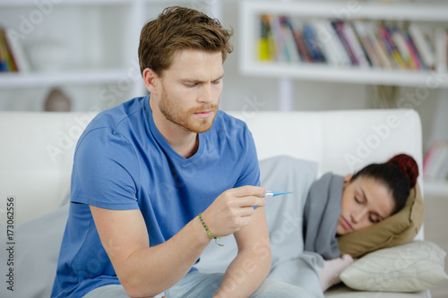 sick woman with boyfriend monitoring her temperature with thermometer