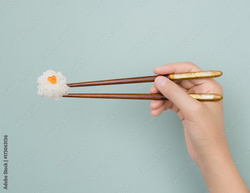 a hand holding a bite size rice with chop stick a hand holding a bite size rice with chop stick