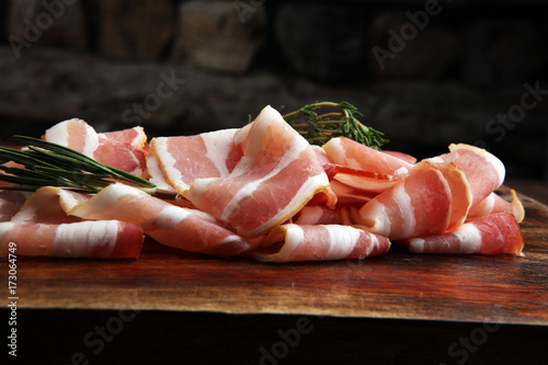 Raw sliced bacon with thyme leaves ready for cooking.