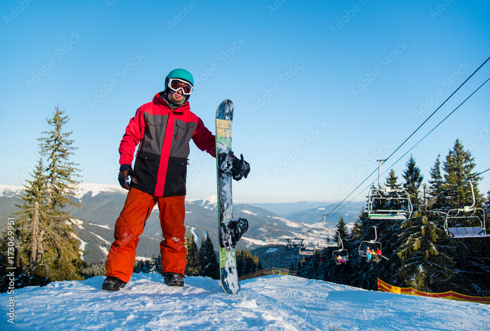 Full length shot of a snowboarder standing with his snowboard on the top of  the mountain
