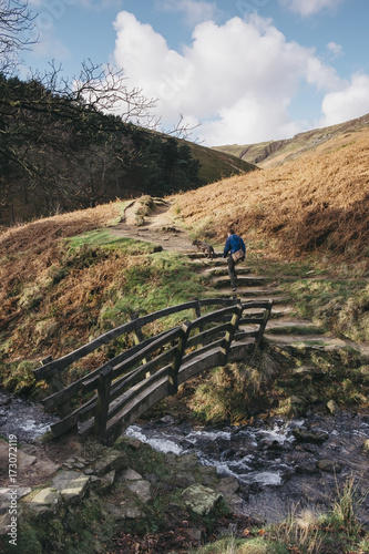 Male and his dog crossing an old wooden bridge on a hillside. Edale, Derbyshire, UK. photo