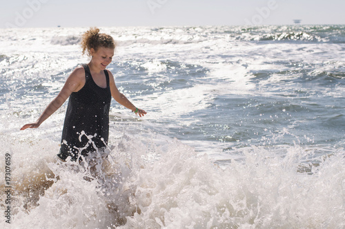 Young girl stands in waves at sea on a clear sunny day