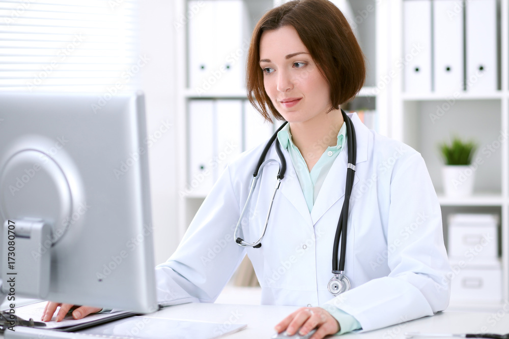 Young brunette female doctor sitting at the table and working at hospital office. Young brunette female doctor sitting at the table and working at hospital office.