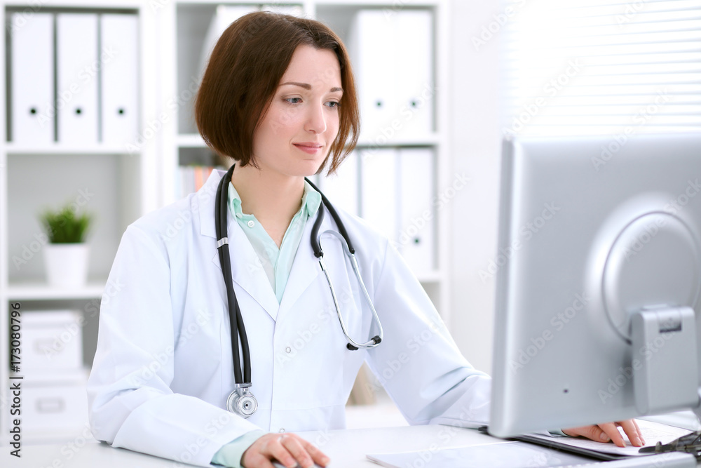 Young brunette female doctor sitting at the table and working at hospital office. Young brunette female doctor sitting at the table and working at hospital office.