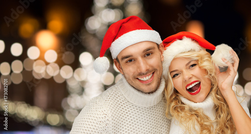 happy couple in santa hats over christmas lights