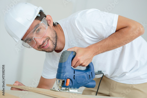 young male carpenter cutting wood with bandsaw in workshop photo