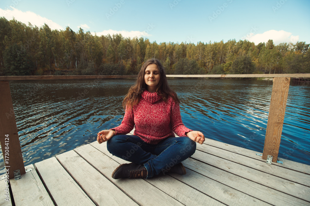 girl in sweater sitting on the pier in the park and meditating