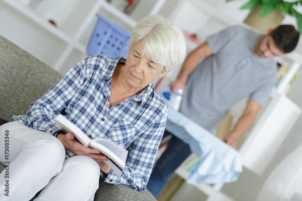 Obraz premium lady reading a book while home help assistant is ironing