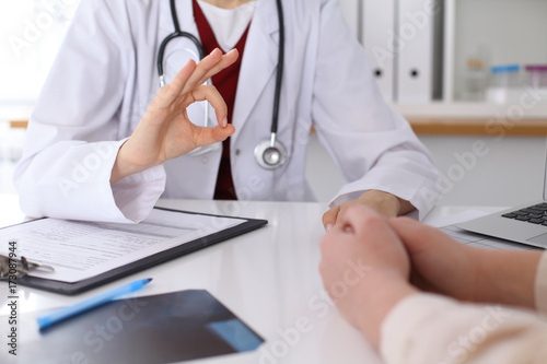 Close up of a doctor hand showing ok sign while phusician and his patient discussing medical records after health examination
